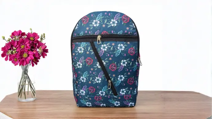 Navy blue backpack with an all-over floral pattern in red, purple, and white, featuring a unique diagonal front zipper and black trim, ideal for fashion or casual use.